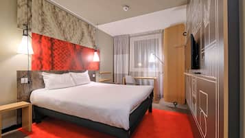 A hotel room with a bed, bedside tables, a desk, a chair, a TV, and a wardrobe.