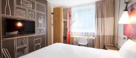 Una habitación de hotel con una cama, un escritorio, una silla, un televisor y una tabla de surf.