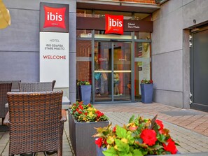 Gevel van een hotel met rieten meubels en potplanten.