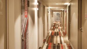 Un pasillo de hotel con piso estampado, puertas a ambos lados y un techo con iluminación empotrada.