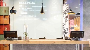 Un mostrador de recepción con dos monitores de computadora, un florero con flores y una pared con texto y un reloj.