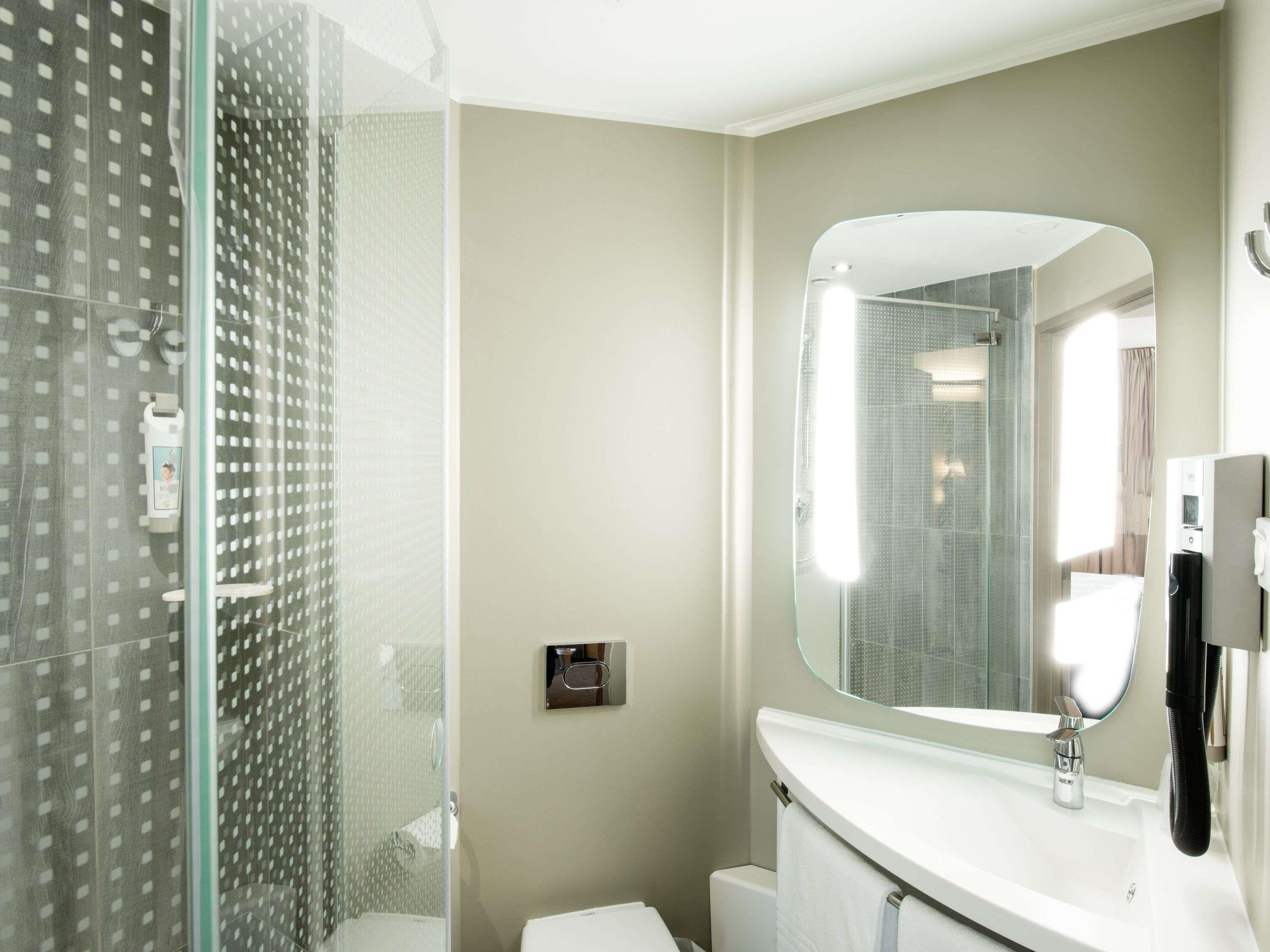 Un baño moderno con cabina de ducha de vidrio, un lavabo blanco con un espejo grande y un inodoro.