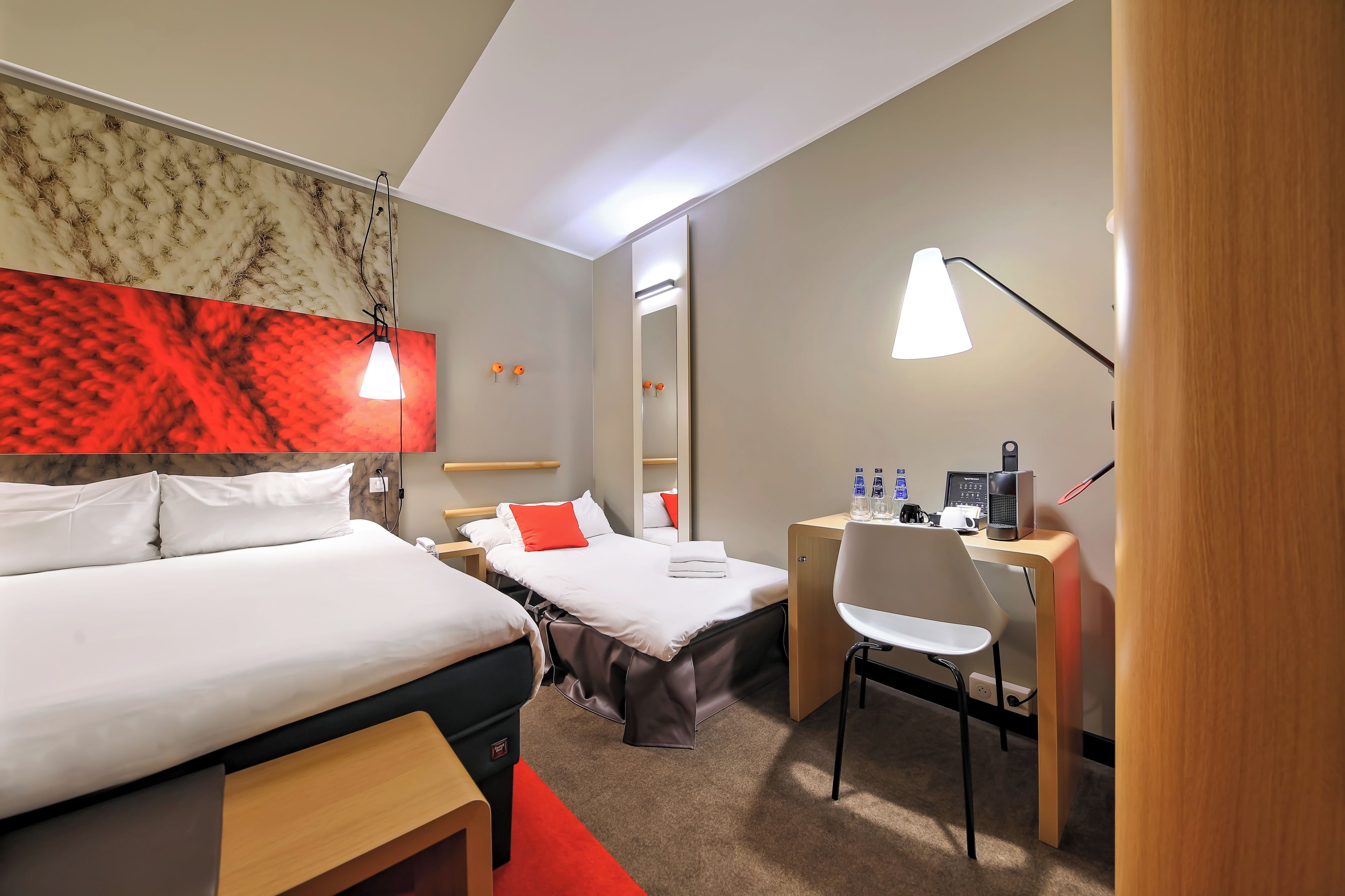 Quarto de hotel com cama, escrivaninha, cadeira e espelho.