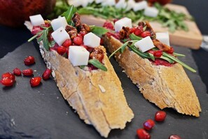 Dos bruschettas cubiertas de queso, nueces y semillas de granada sobre una tabla de pizarra.