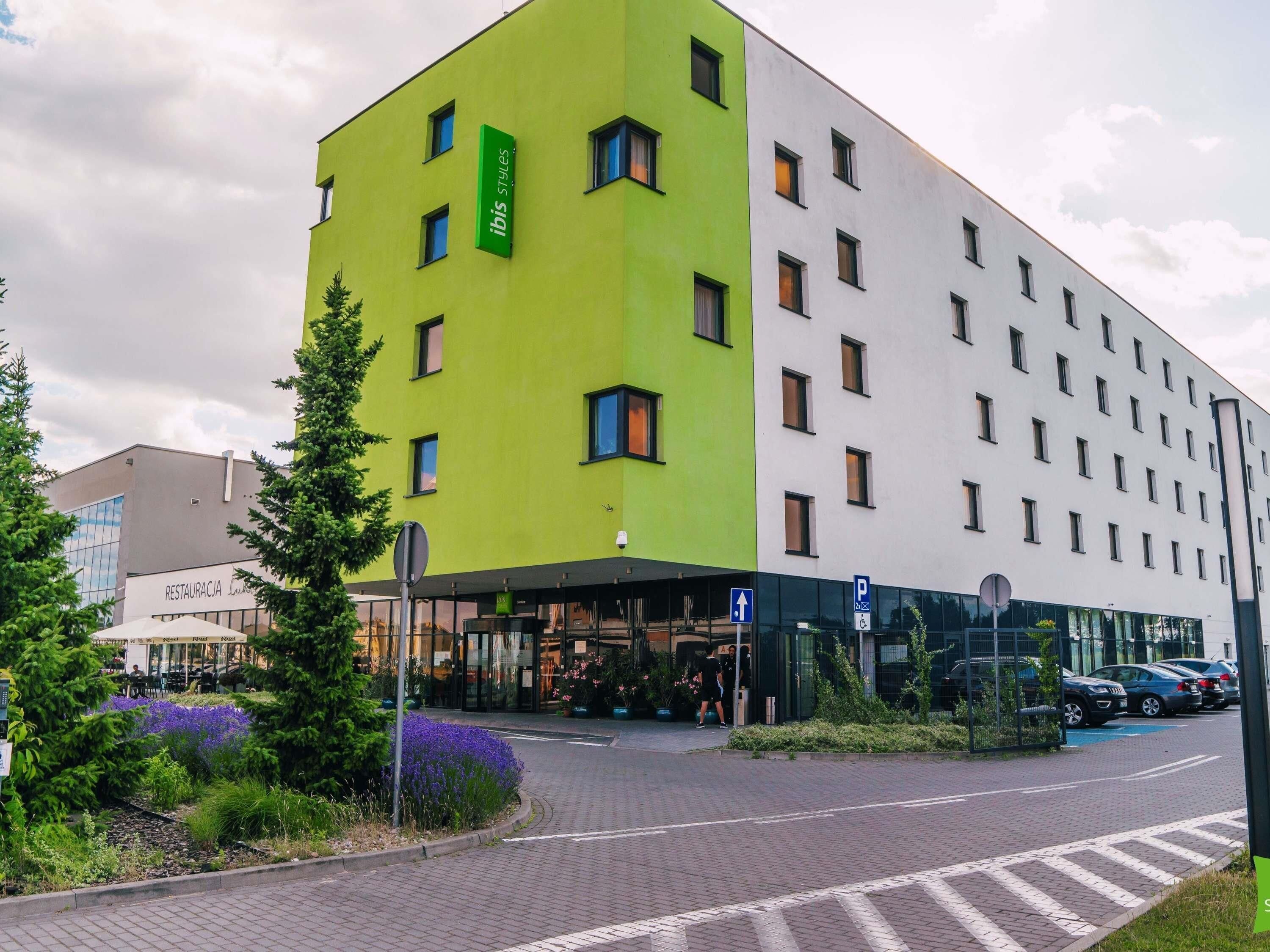 A modern building with a green and white facade, a restaurant entrance, and a parking area.