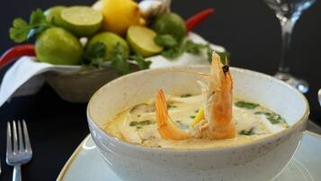 Un tazón de sopa de camarones, adornado con hierbas, y una cesta de verduras al fondo.