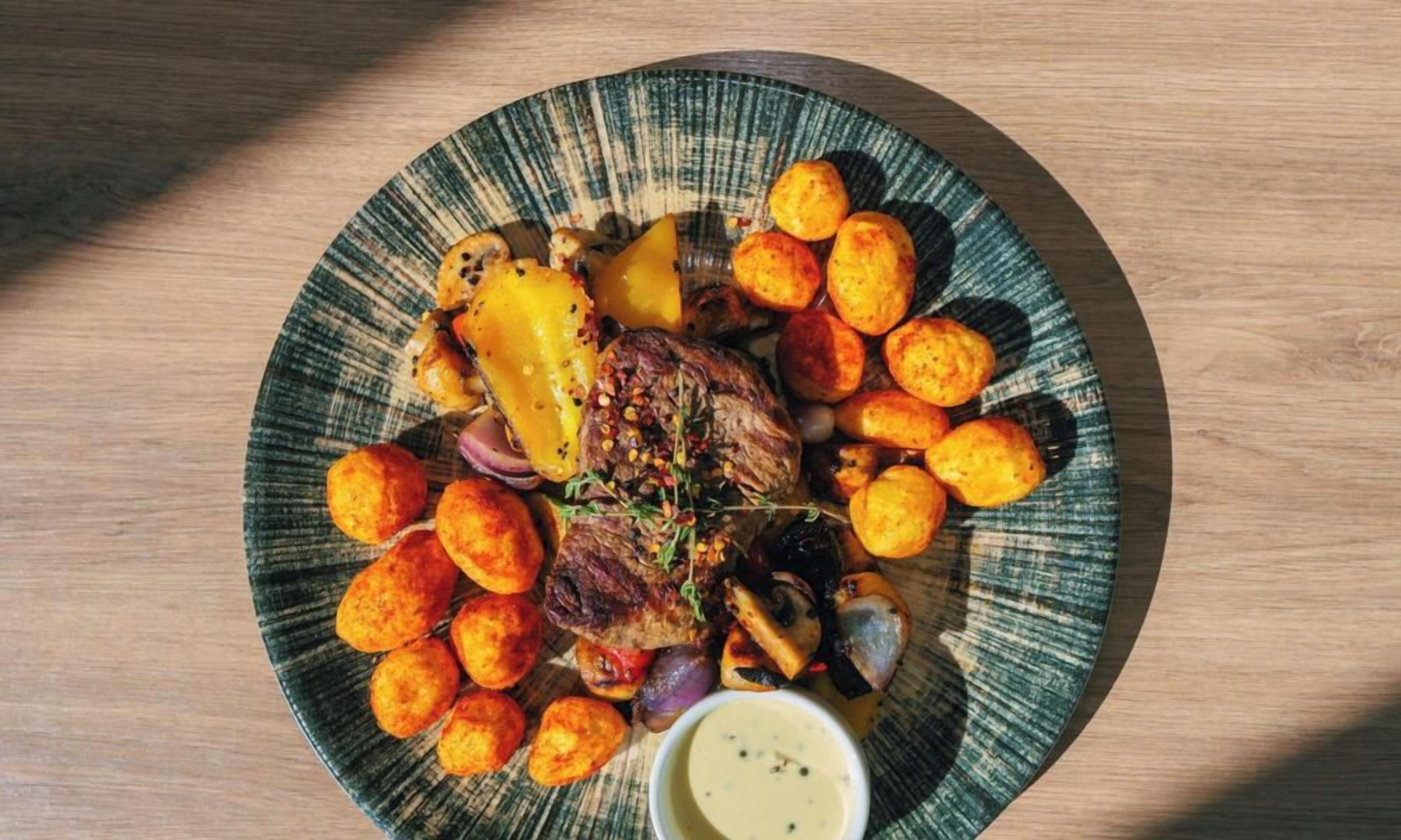 Un plato de comida con varios elementos, incluyendo un bistec, patatas asadas y una guarnición de salsa.