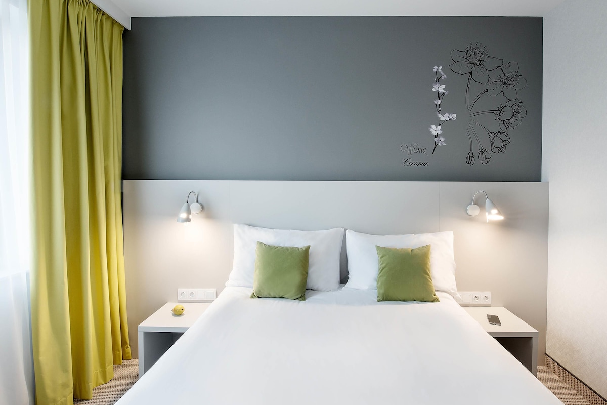 A hotel room with a large bed, two bedside tables, and a wall-mounted light fixture.