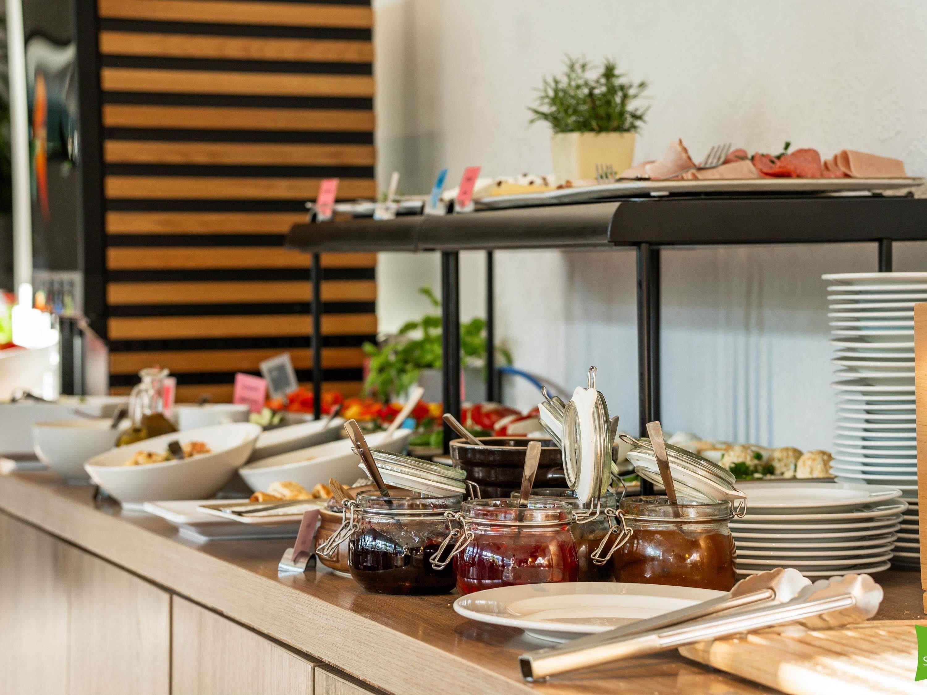 Una mesa de buffet con diversos alimentos, entre ellos botes de conservas, platos y cubiertos.