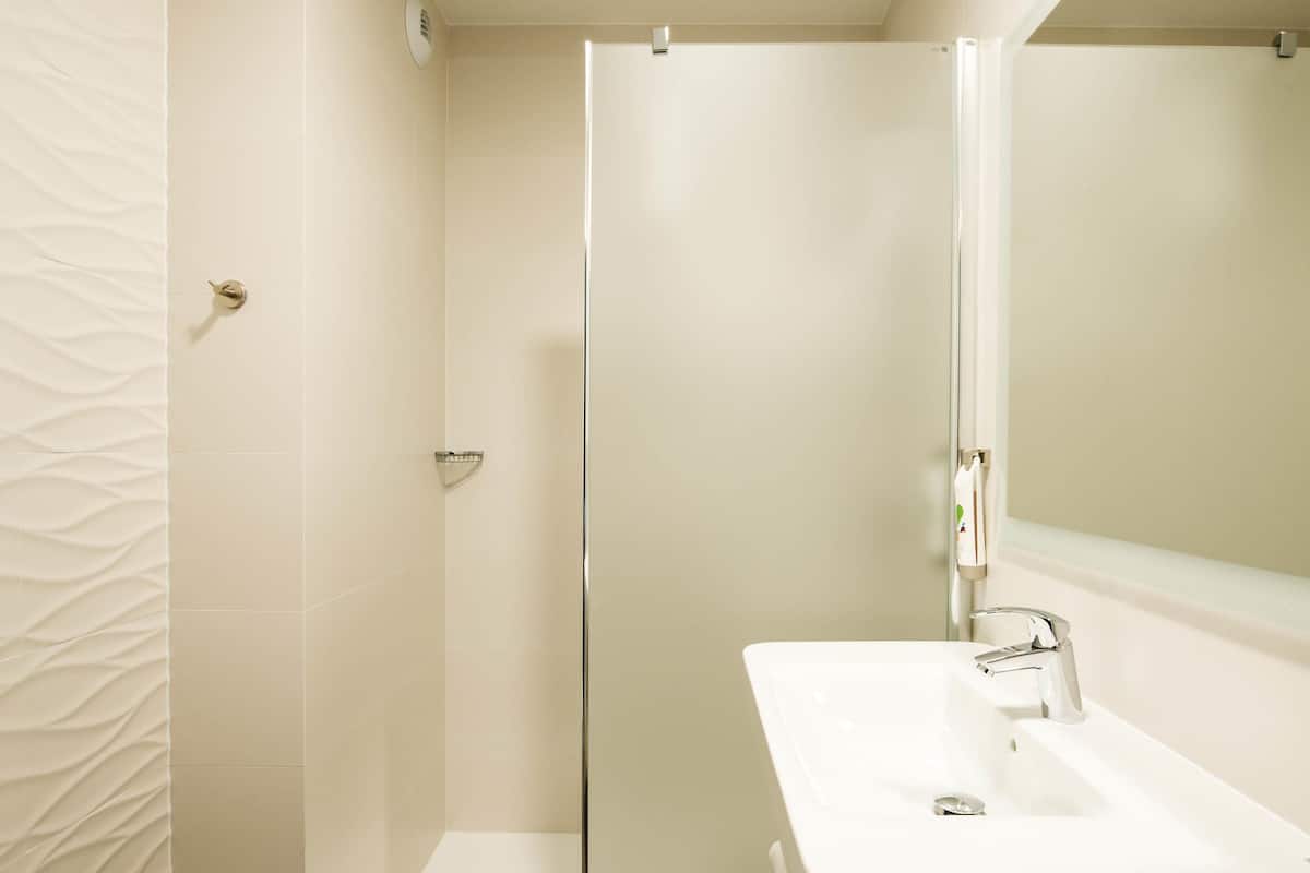Ein Badezimmer mit einem weißen Waschbecken, einer Duschkabine aus Glas und einer Wand mit Struktur.