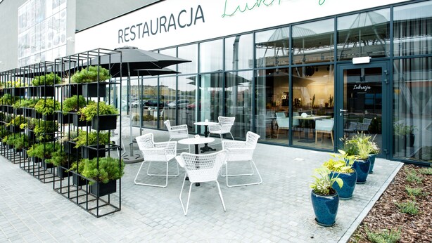 Un restaurante llamado 'RESTAURACJA Lukrecja' con terraza y plantas en macetas.
