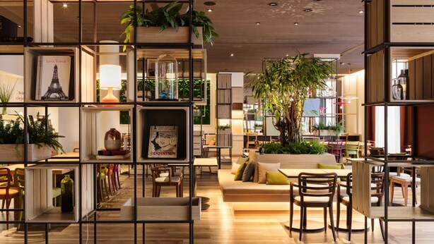 A modern interior with open shelving, seating areas, and indoor plants. - IntercityHotel Braunschweig (Braunschweig)