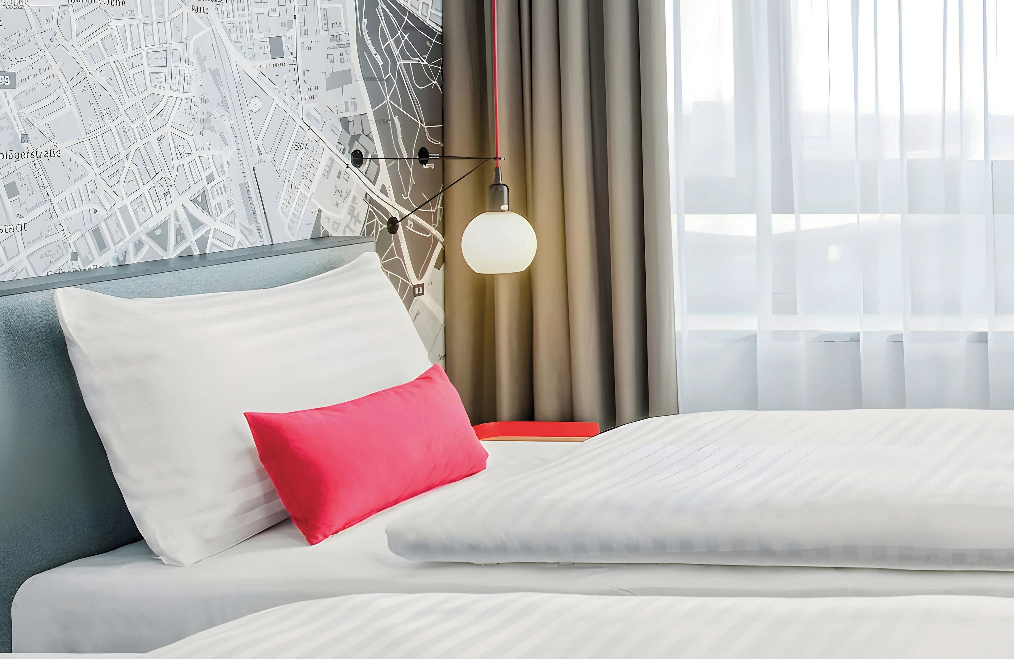 A hotel room with a bed, a map wall, a lamp, and curtains.
