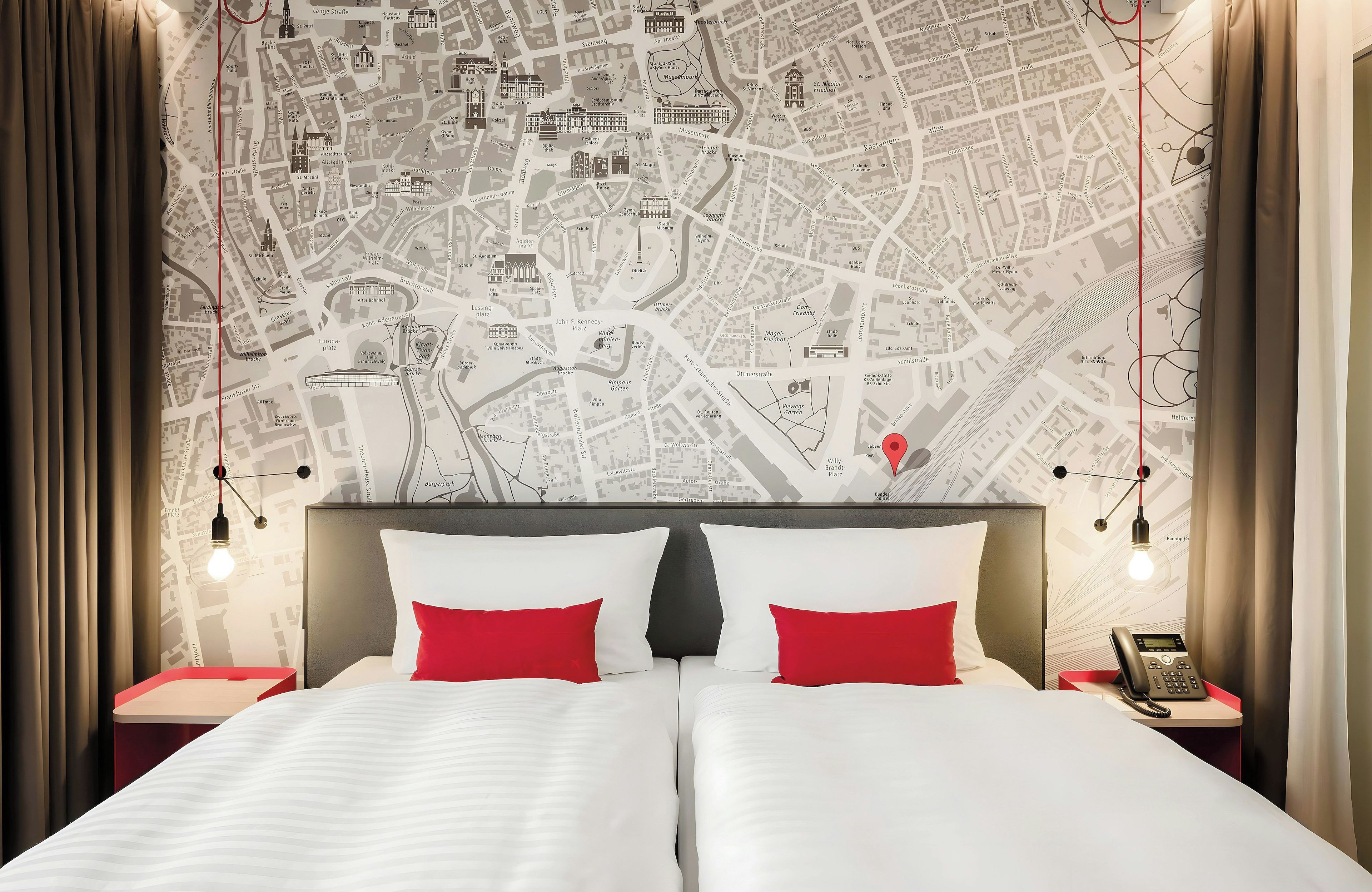 A hotel room with a large bed, two nightstands, a red telephone, and a map of a city on the wall.
