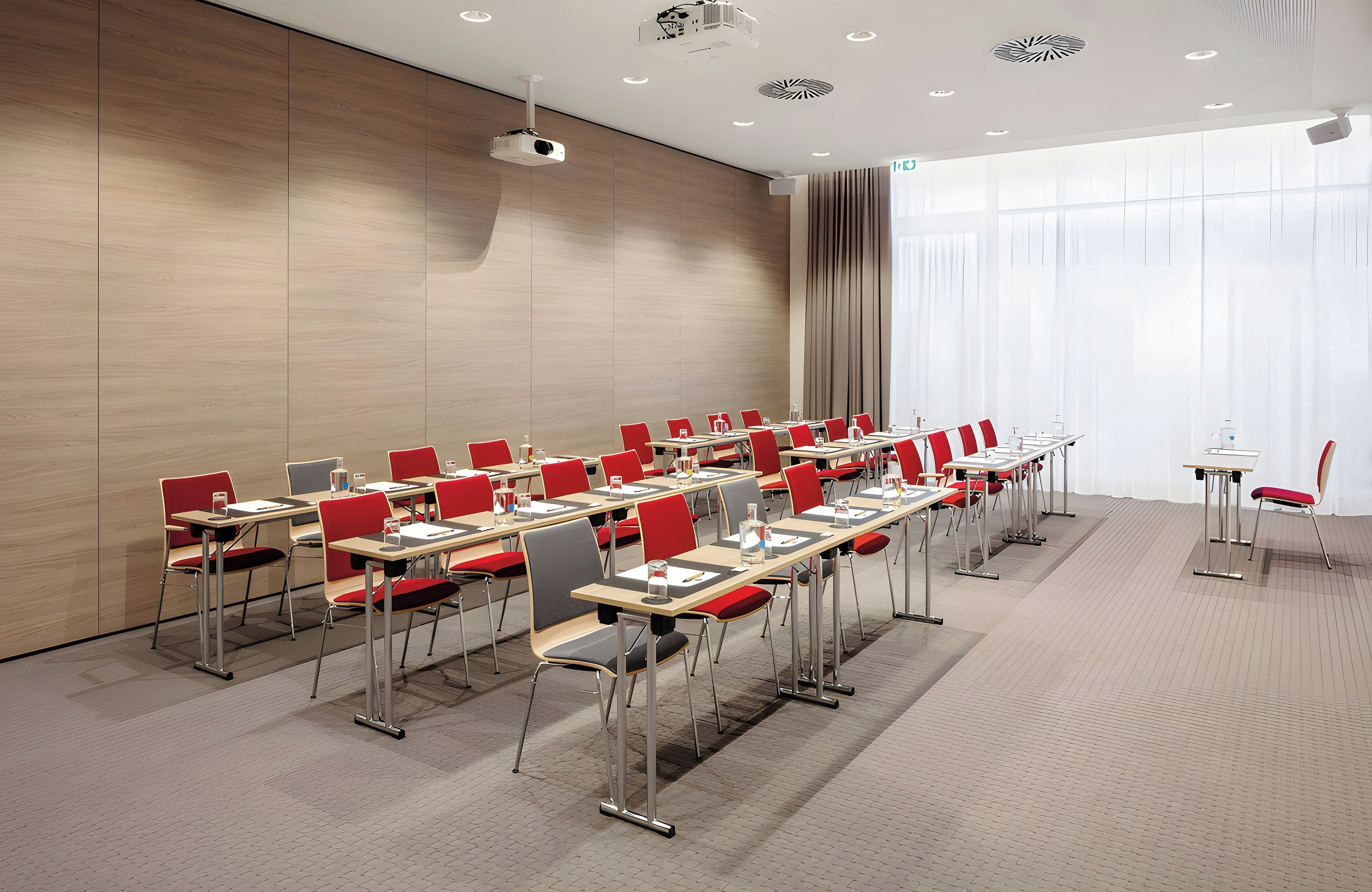 A conference room with rows of tables and chairs, a projector, and a large window with curtains.