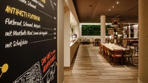 A modern interior with a long dining area, wooden flooring, and a blackboard menu listing food items. - IntercityHotel Braunschweig (Braunschweig)