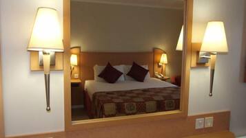A hotel room with a bed, two bedside lamps, and a mirror above the bed.