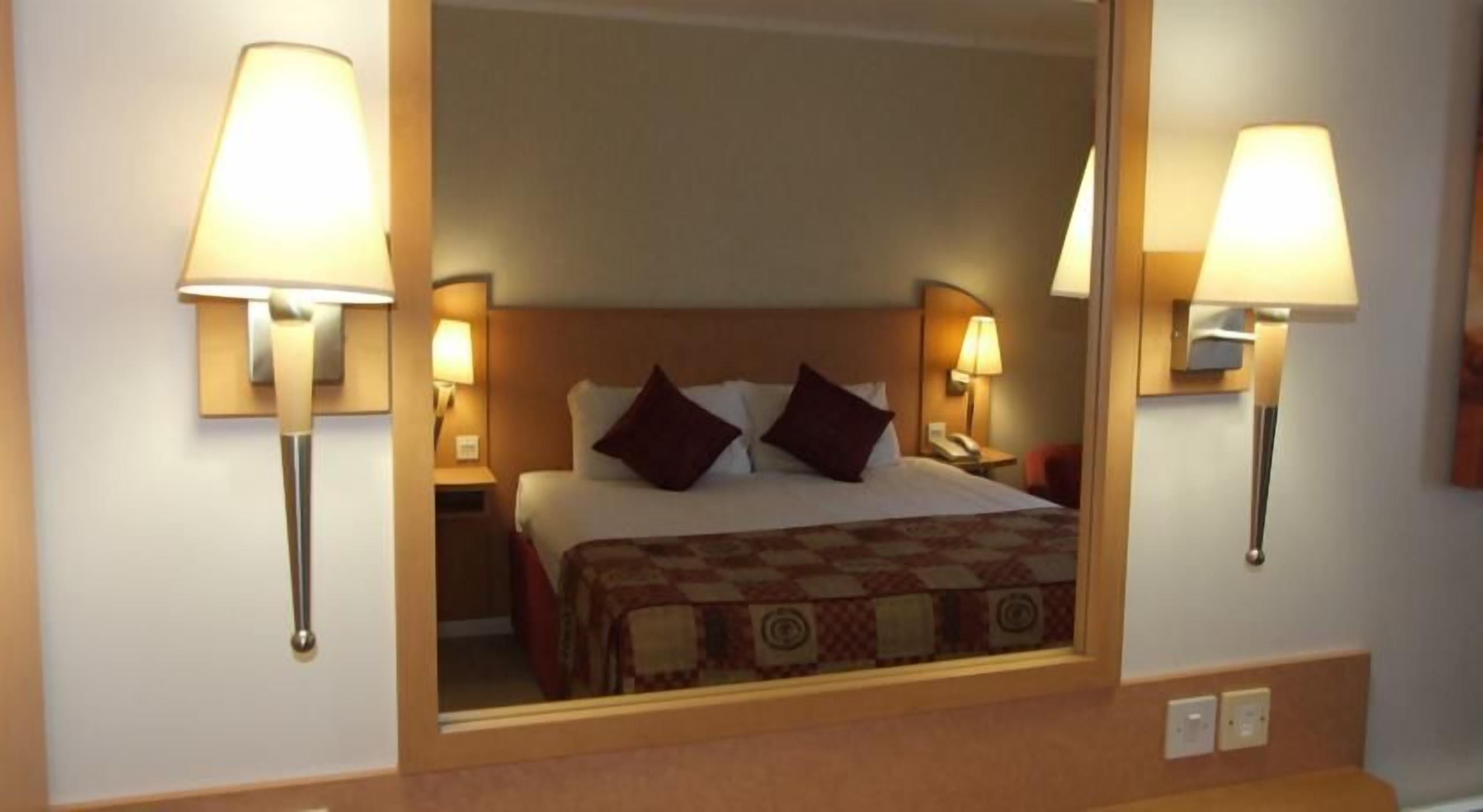 A hotel room with a bed, two bedside lamps, and a mirror above the bed.