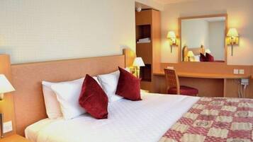 A hotel room with a bed, a desk, a chair, a mirror, and two wall-mounted lamps.