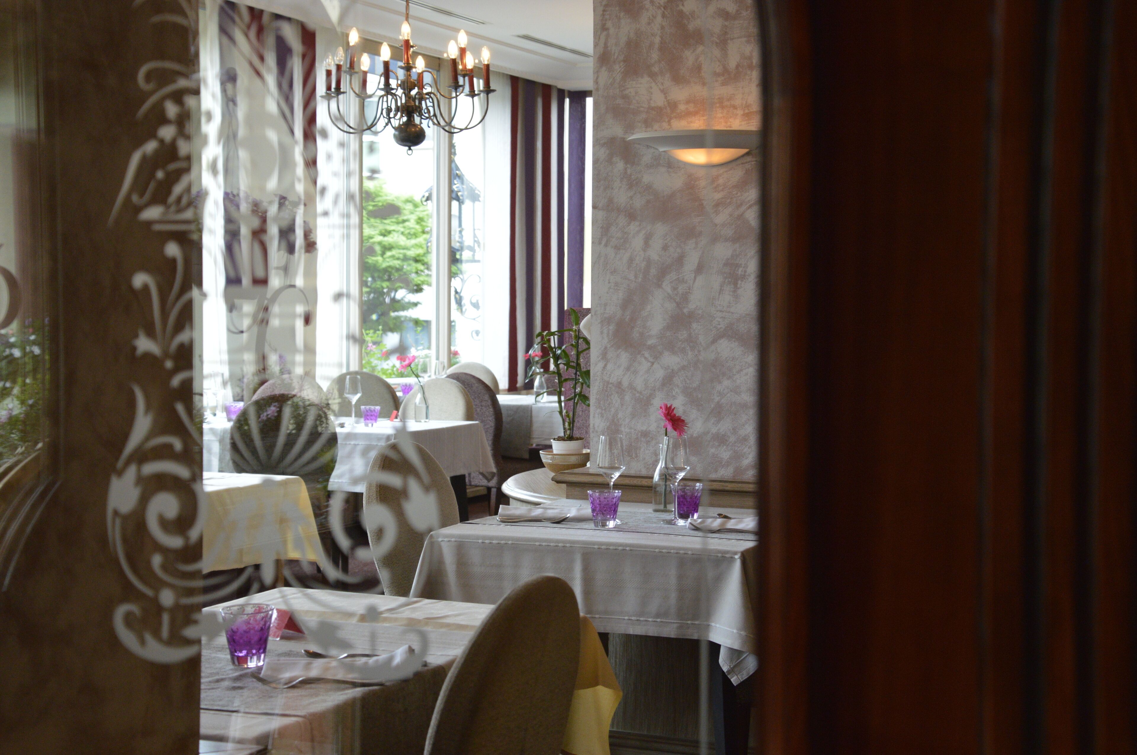 A restaurant with tables set for dining, a chandelier, and a view of the outdoors.