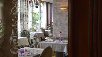 A restaurant with tables set for dining, a chandelier, and a view of the outdoors.