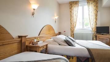 Ein Hotelzimmer mit zwei Betten, einem Holz-Kopfteil, einem Nachttisch mit Lampe, einem Fernseher und einem Fenster mit Vorhängen.