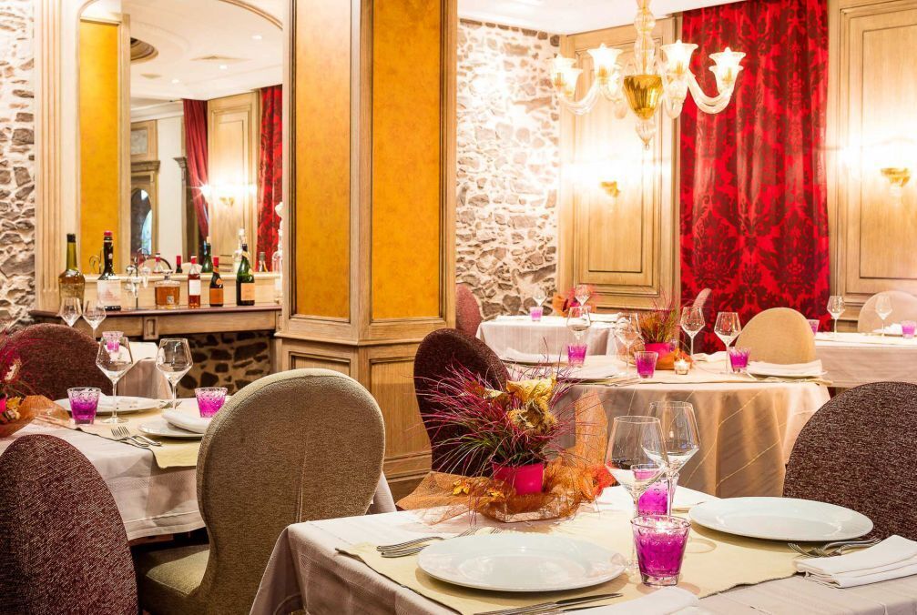 A dining area with tables set for a meal, featuring a stone wall and red curtains.