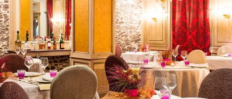 A dining area with tables set for a meal, featuring a stone wall and red curtains.