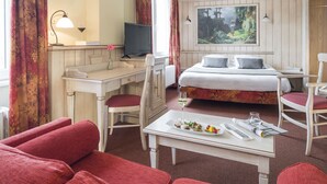 A hotel room with a bed, a desk with a computer, a dining table with a plate of food, and a painting on the wall. - Hotel Restaurant Le Bristol (Niederbronn-les-Bains)