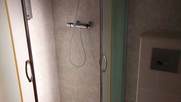 Une cabine de douche fermée par des parois en verre, dotée d’un pommeau de douche à main et d’un panneau de commande fixé au mur.