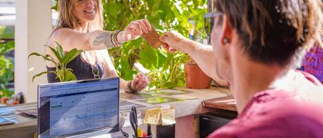 A person handing over a card to another person at a counter with a laptop, plants, and notes visible.