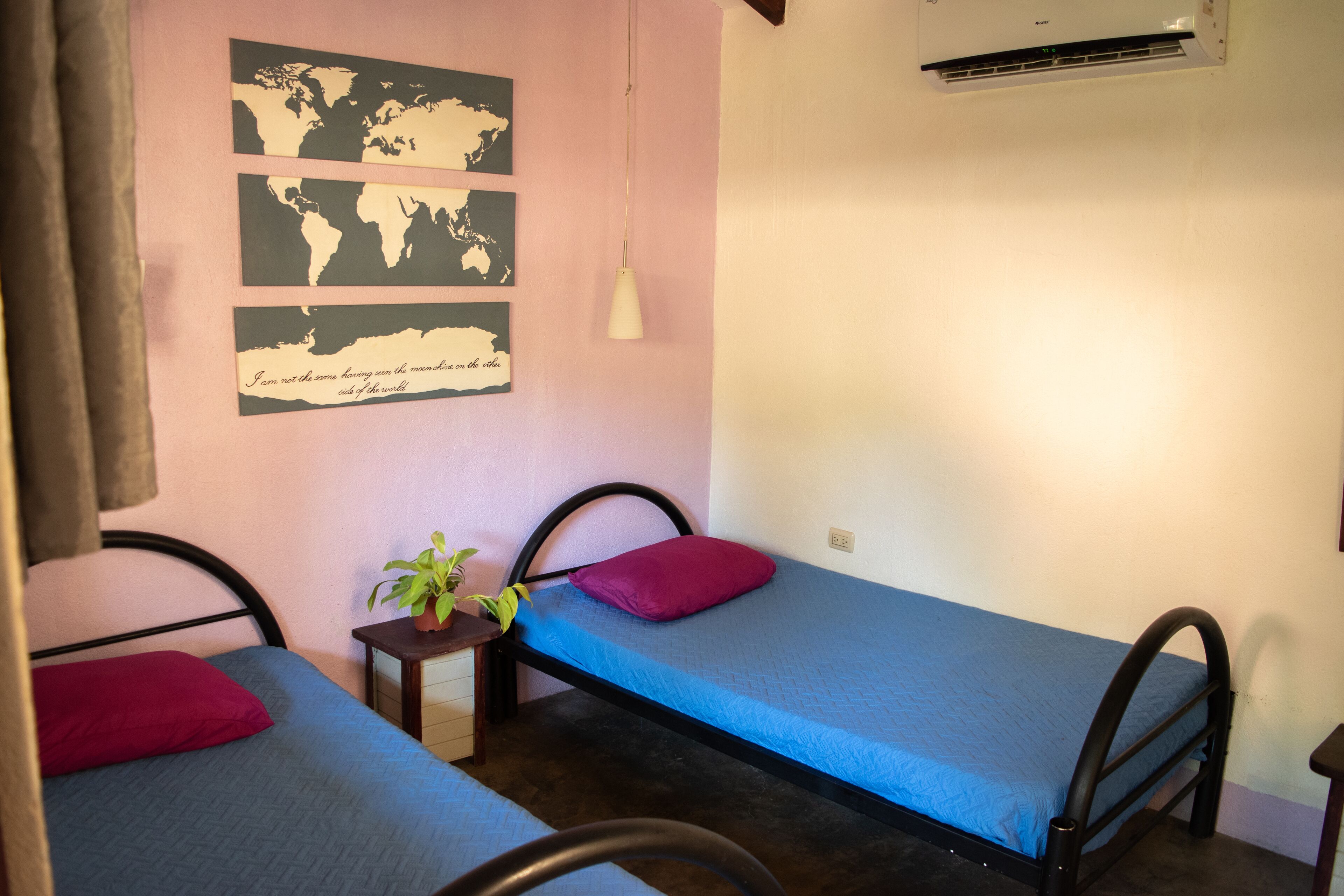 A small, cozy room with two single beds, a small table with a plant, and a world map on the wall.