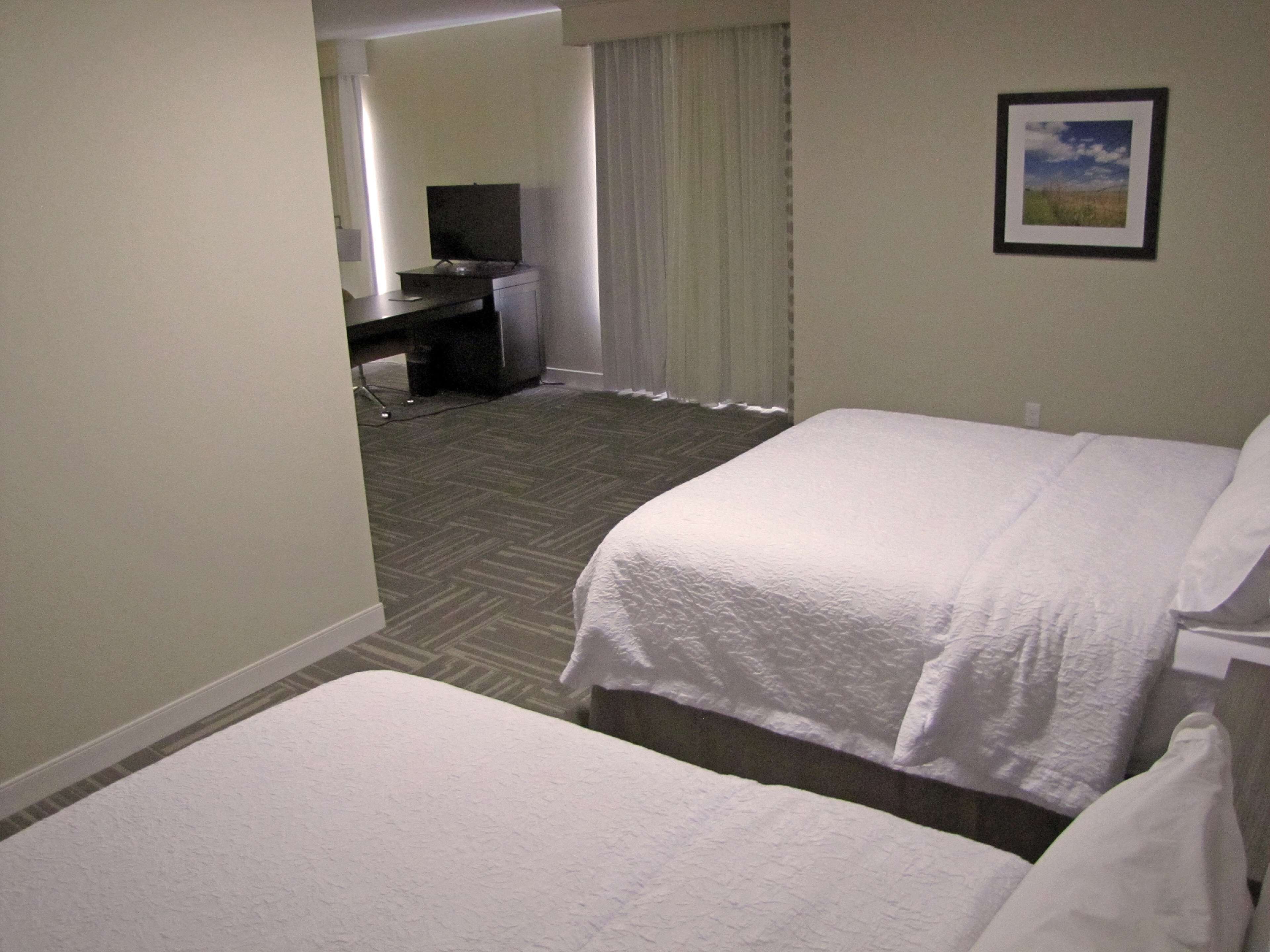 A hotel room with two beds, a desk, a chair, and a television.