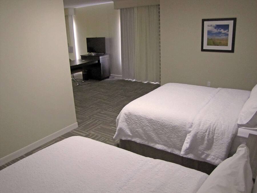 A hotel room with two beds, a desk, a chair, and a television.