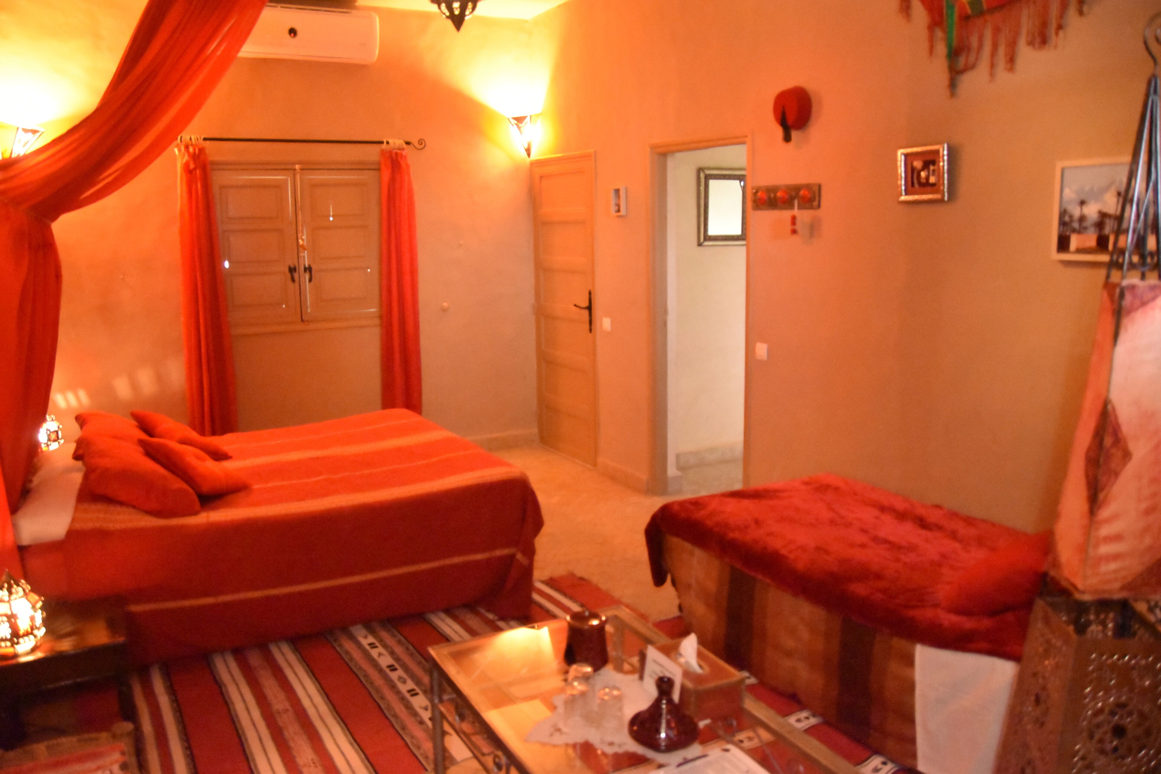 A room with a bed, a small table with a lamp, and a bench.