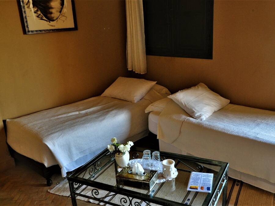 A hotel room with two single beds, a small table with a tray, a vase with flowers, and a framed picture on the wall.