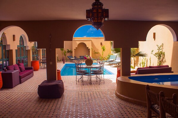 An indoor pool area with a table and chairs, surrounded by arches and potted plants.