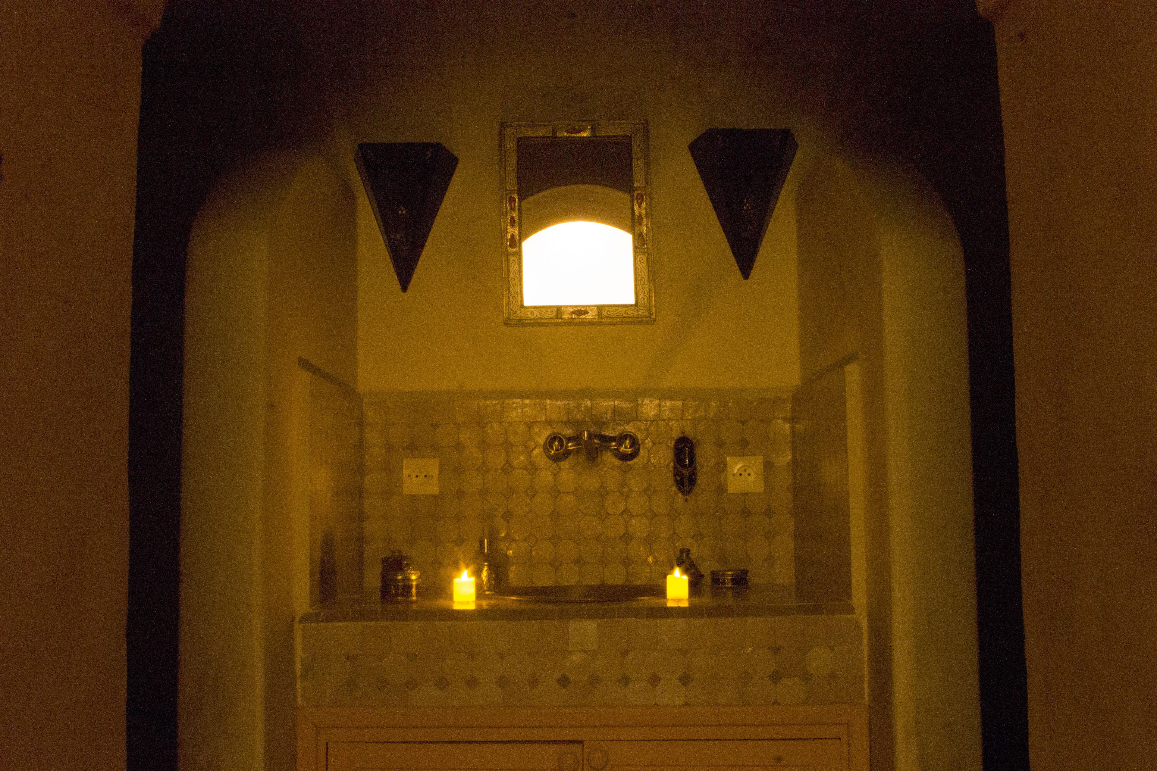 Une salle de bain avec un mur recouvert de carreaux, un miroir et deux appliques murales.