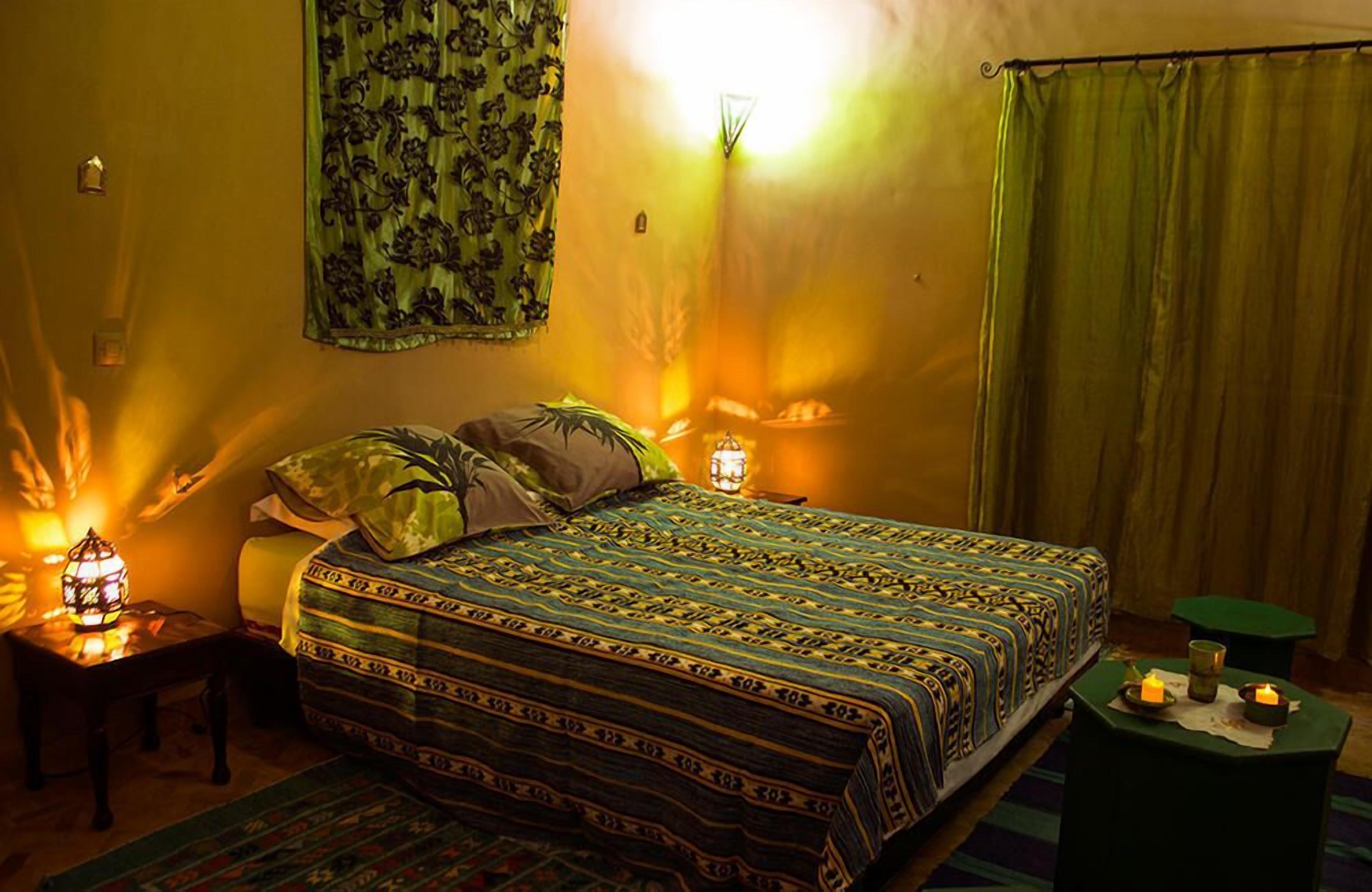 Ein gemütliches Schlafzimmer mit einer gemusterten Tagesdecke, einem grünen Vorhang und einem kleinen Tisch mit Kerzen.