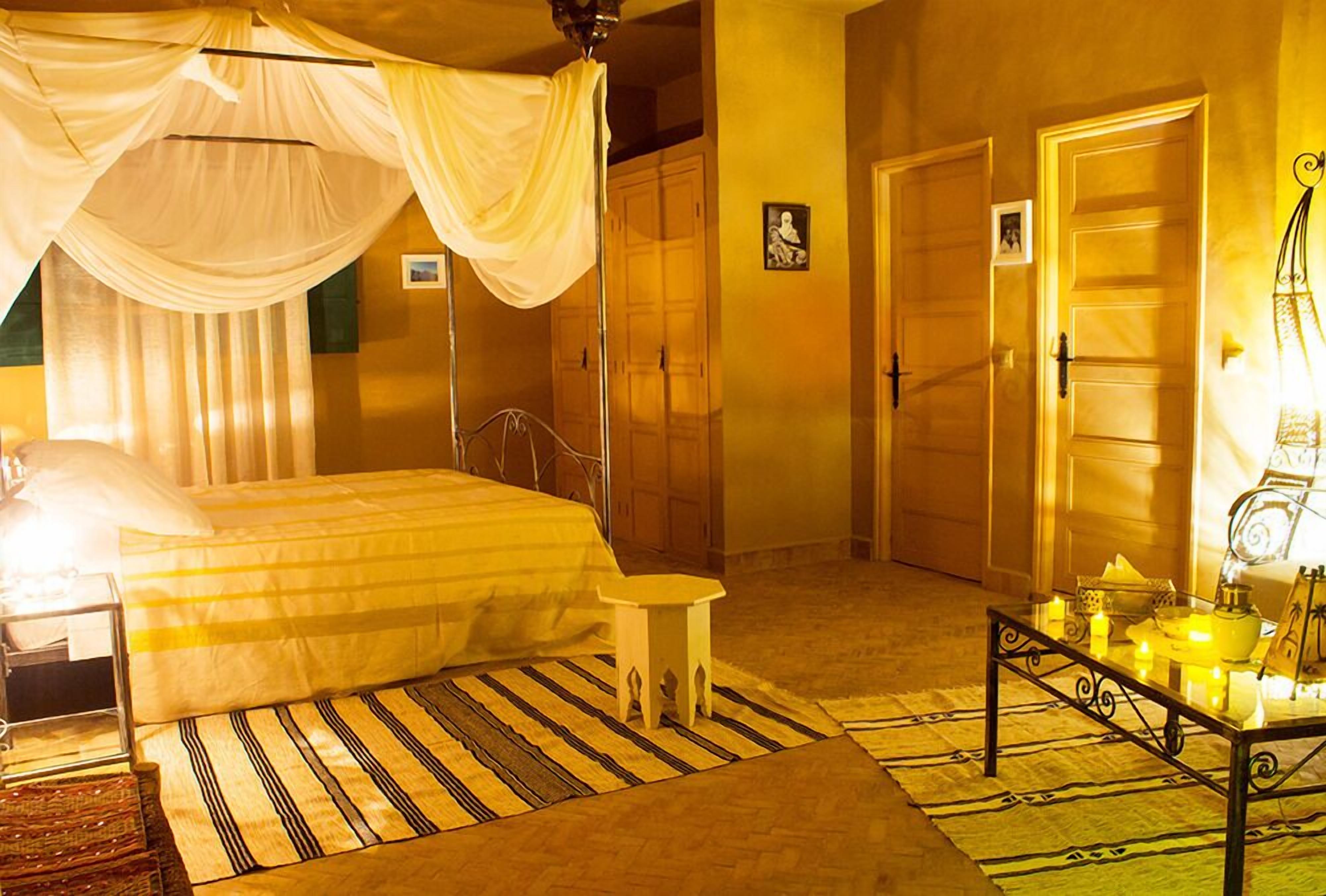 A bedroom with a bed, a nightstand, a bedside table with candles, and a window with curtains.
