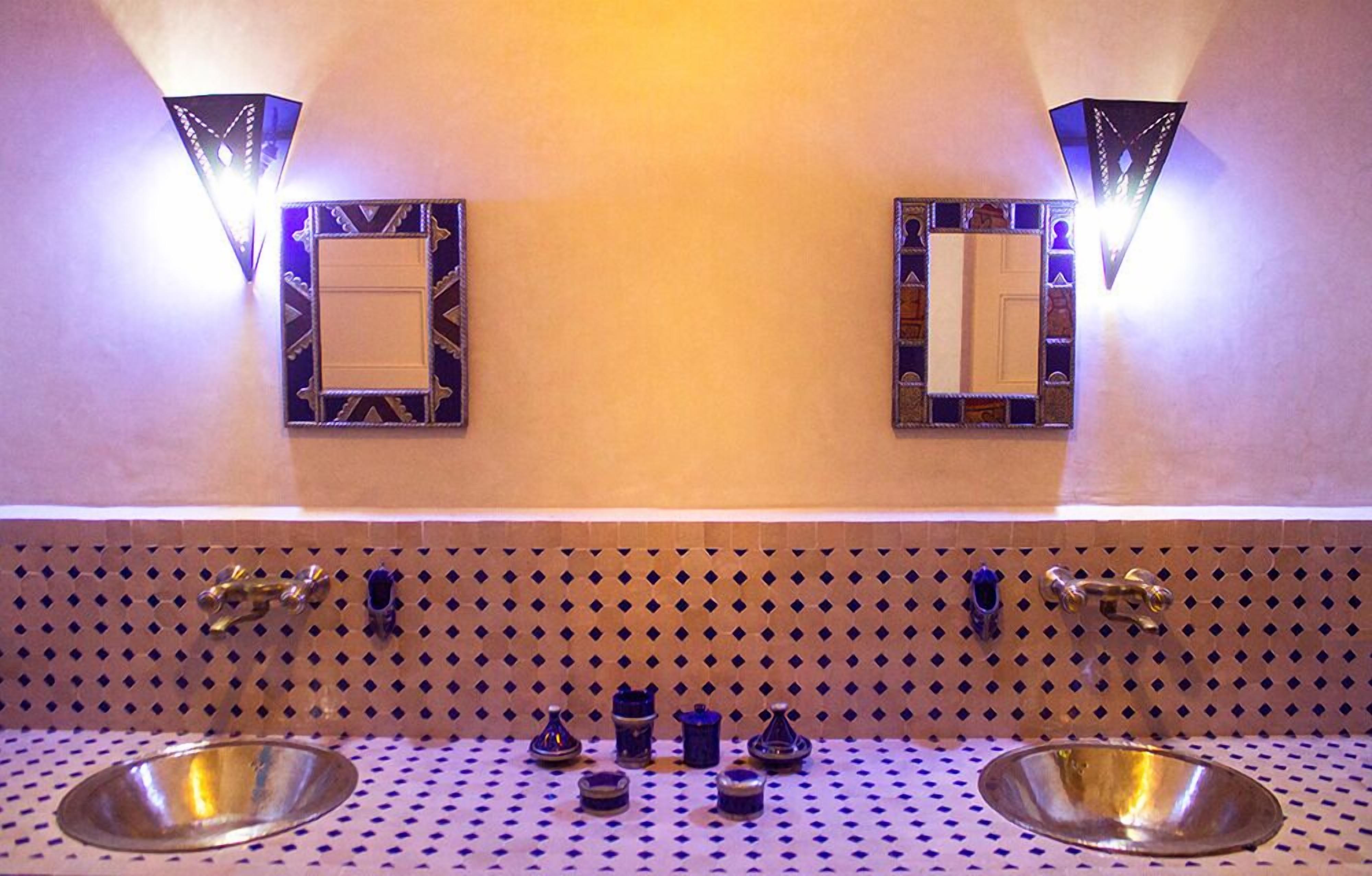 Un baño con dos lavamanos, apliques decorativos en la pared y un salpicadero de azulejos estampados.
