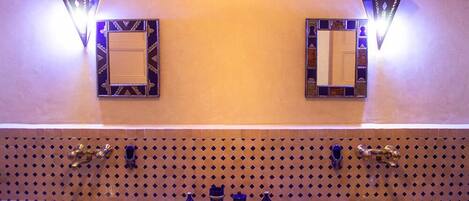 Un baño con dos lavamanos, apliques decorativos en la pared y un salpicadero de azulejos estampados.