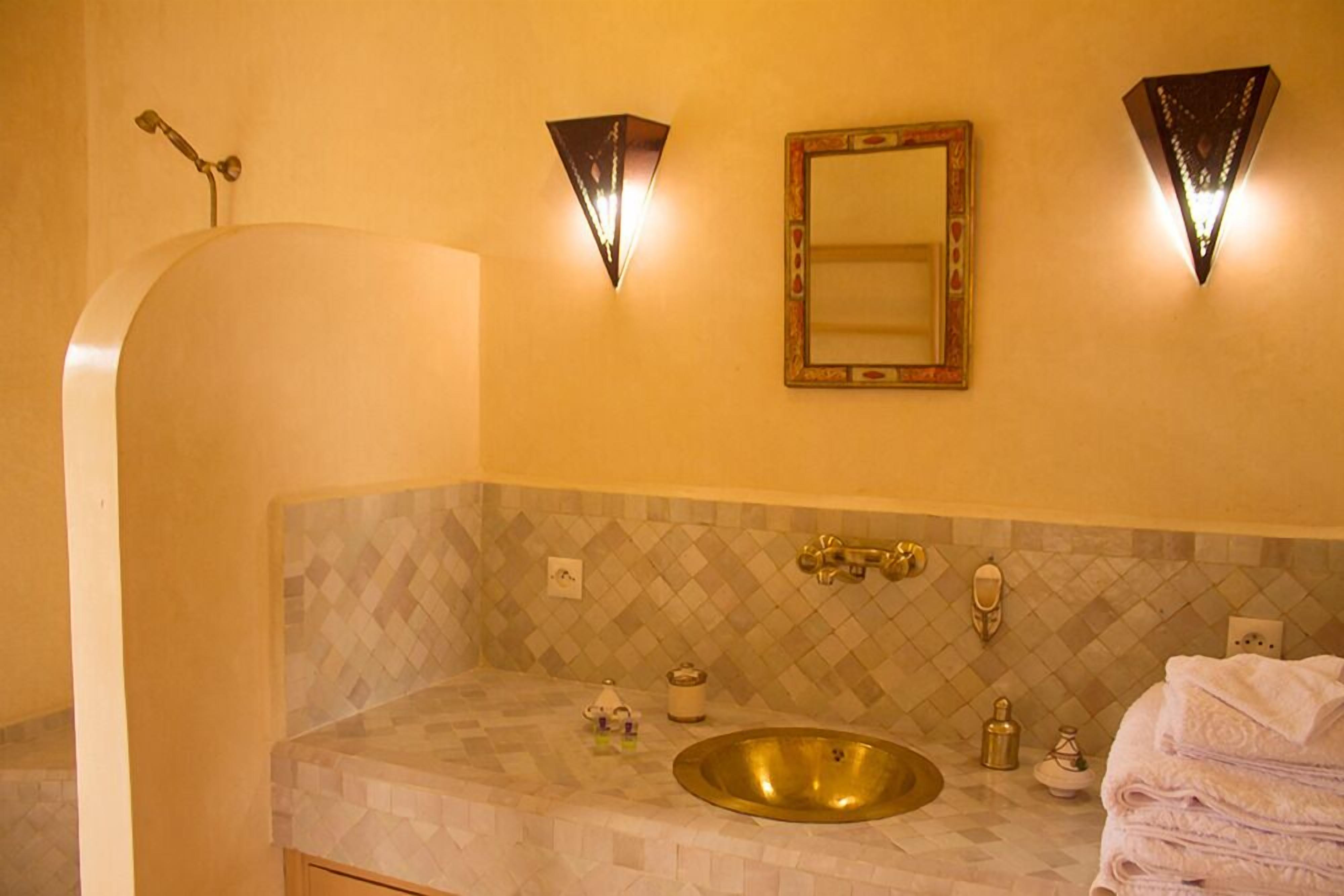 A bathroom with a freestanding bathtub, a sink with a gold basin, and two wall-mounted lights.