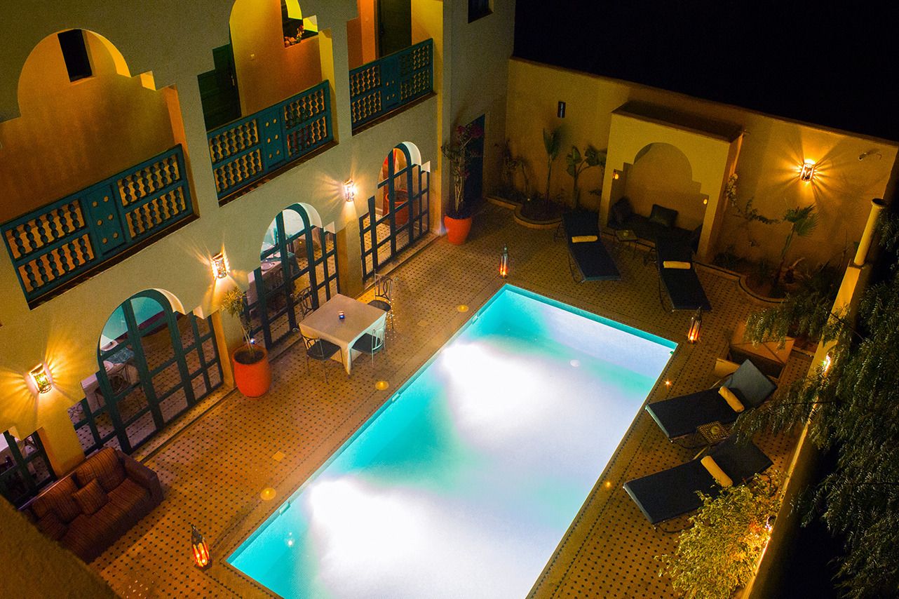 A rooftop pool area with lounge chairs, a table, and potted plants.
