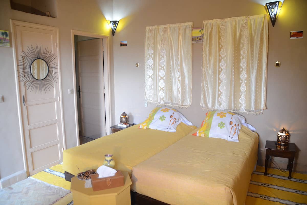A double bed with two pillows, a nightstand with a lamp, a mirror on the wall, and a door leading to another room.