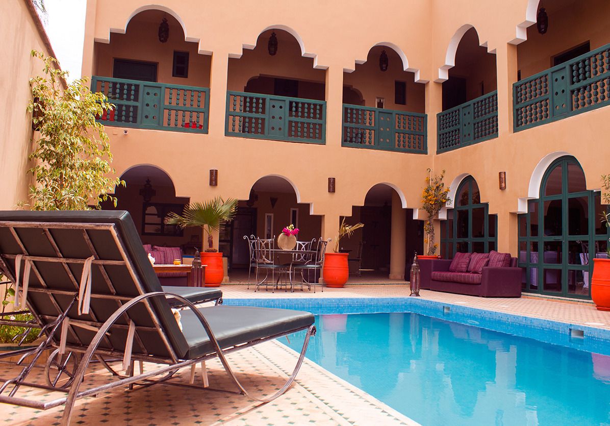 Un área de piscina con sillas de descanso y un sofá, rodeada de arcos y un suelo con mosaicos.