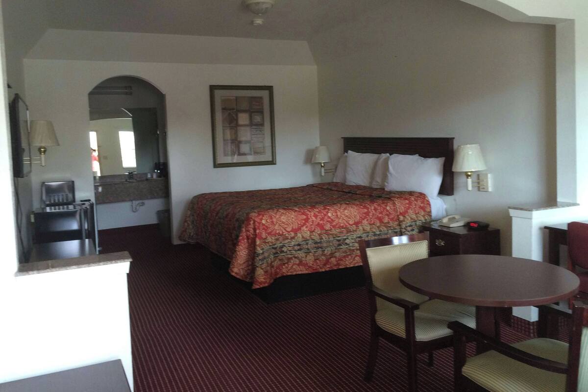 A hotel room with a bed, a desk, a chair, a table, a lamp, and a mirror.