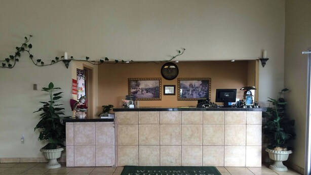 A reception desk with a welcome mat, potted plants, a clock, framed pictures, and a computer monitor. - Executive Inn & Suites Schulenburg (Schulenburg)