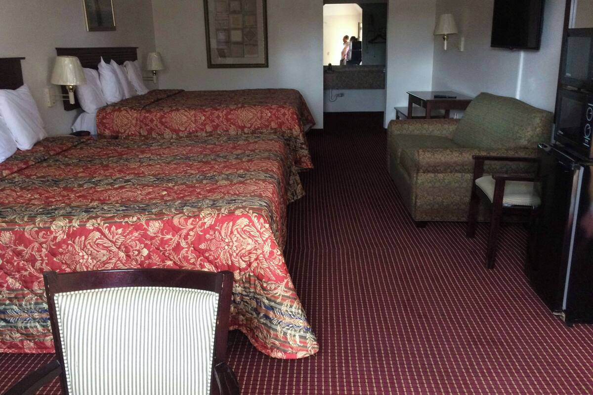 A hotel room with two beds, a chair, a television, and a desk.