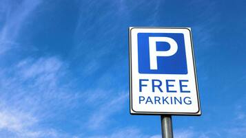Un panneau de signalisation indiquant un parking, avec un « P » bleu et les mots « PARKINGS GRATUITS » sur un fond de ciel bleu clair.